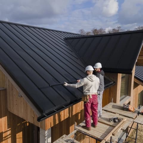 Deux couvreurs installant une toiture métallique sur un chantier, illustrant la gestion du temps et du planning avec Tim Management.